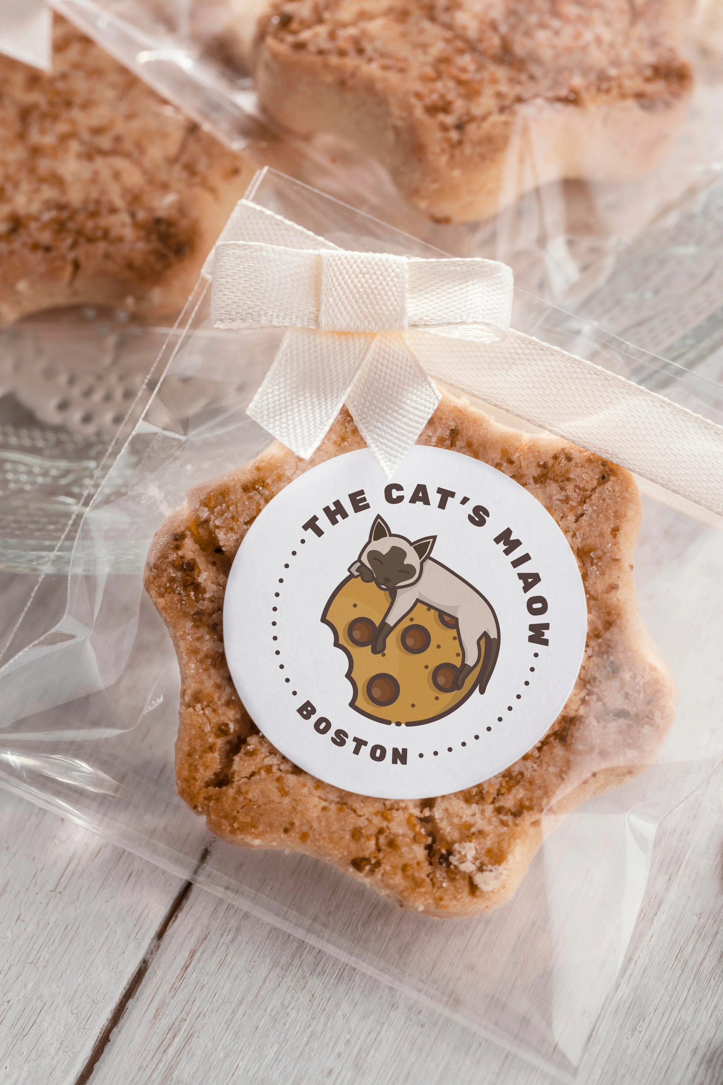 Cookie in a clear cellophane bag with a white ribbon and a round label with a cat peeking over a slice of pizza. The label reads 'The Cat's Mawow Boston'.