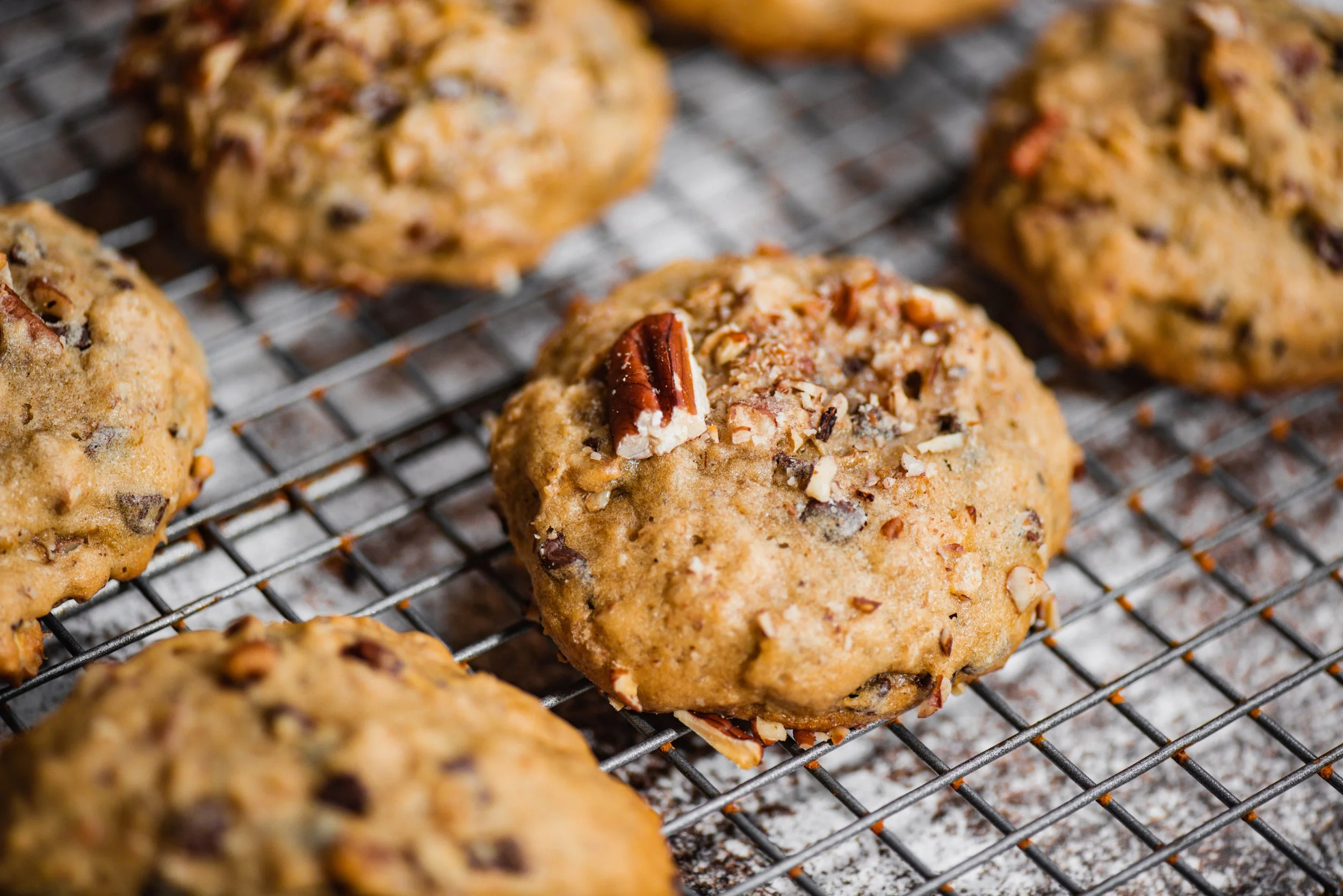 Close-up of freshly baked chocolate chip cookies on a cooling rack with some crushed nuts on top.