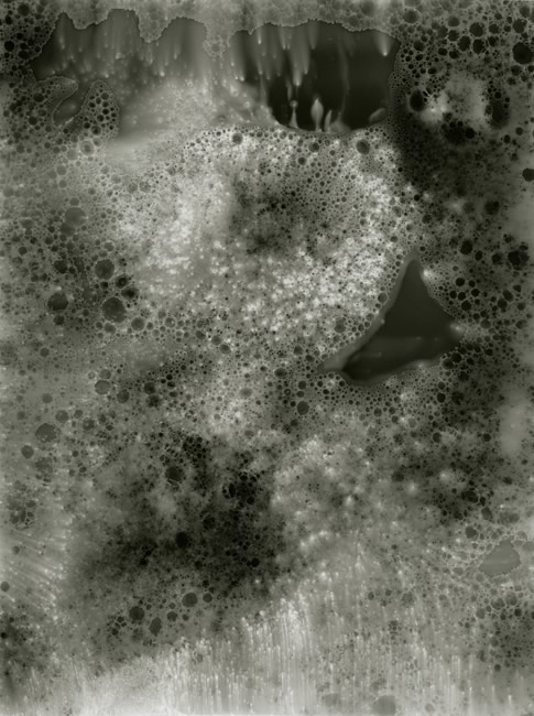 Normandy/Paris, June 2013, no. 1 2013 silver gelatin print photogram 16 inches x 12 inches unique Portfolio for Dust: Plates of the Present, Paris Normandy/Paris, June 2013, no. 1 - 8 This series of photograms was started in Normandy, when I was visiting friends, and where I was to visit the grave of my uncle who died there in World War II. I had never met my uncle, as I had not been born yet. I had heard a few stories about him, scraps of other family members’ memories— that he was a dapper dresser, and an excellent waiter in the family restaurant, that he was my mother’s favorite brother, that he was a photographer and a journalist, and that my grandparents were heartbroken when they received the telegram. To my knowledge, besides one of his brothers, my uncle, no one else had been able to visit his grave. Looking out at the site — a very flat, long, wide sandy beach— it seemed miles before it met the water. I could only imagine the impossibility of its efficacy in wartime; there was no cover. Its constant movement could not erase its history—oscillating between the beautiful and the terrible. It was this constant opposition that I wanted to somehow capture in the photograms: the movement of the salt water washing over the sandy beach in darkness exposed by a searching flashlight. There was one problem: in my haste to make the train from Paris to Normandy I forgot the photo paper. I went looking for some. There were no stores, or time for shipping, but my friend’s friend said her brother was a photographer and she gave me two old boxes of photographic paper. That night, on the beach, when I went to take out the first sheet of paper, I found that the box was empty. The second box had only three scraps of paper— not unlike the scraps of what I knew about my uncle. The photograms made on the three scraps became just a hint of what was lost. Back in Paris, I decided to try to make the photograms from similar substances and particles, changeable and continually in motion-- constantly moving salt water and sand, in darkness exposed to a moment of light in an ocean concieved in the darkroom. The resulting series of photograms are unique, unable to be duplicated—the opposite of a photograph.
