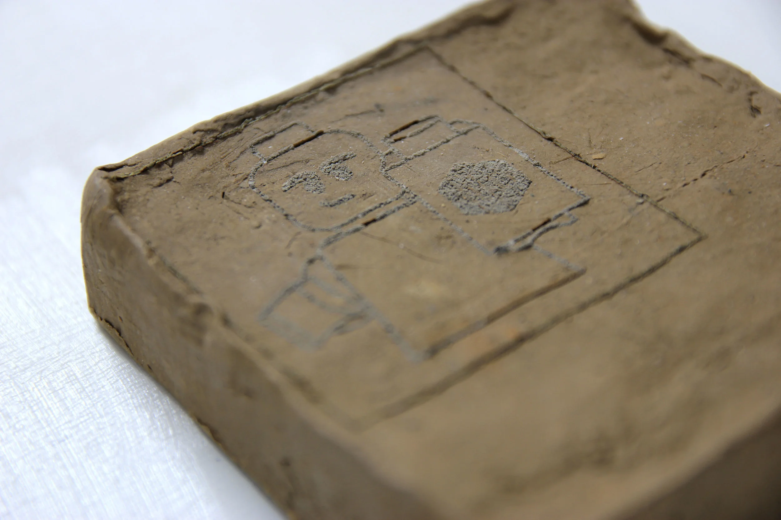 Laser etching onto dug-up mud, likely with a reasonably high clay content (and yes that is a LEGO figure).