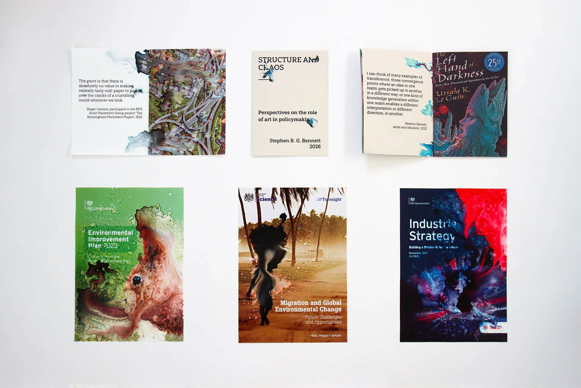 Structure and Chaos artist book displayed with open spreads and altered prints based on government reports including the Environmental Improvement Plan, Migration and Global Environmental Change and Industrial Strategy.
