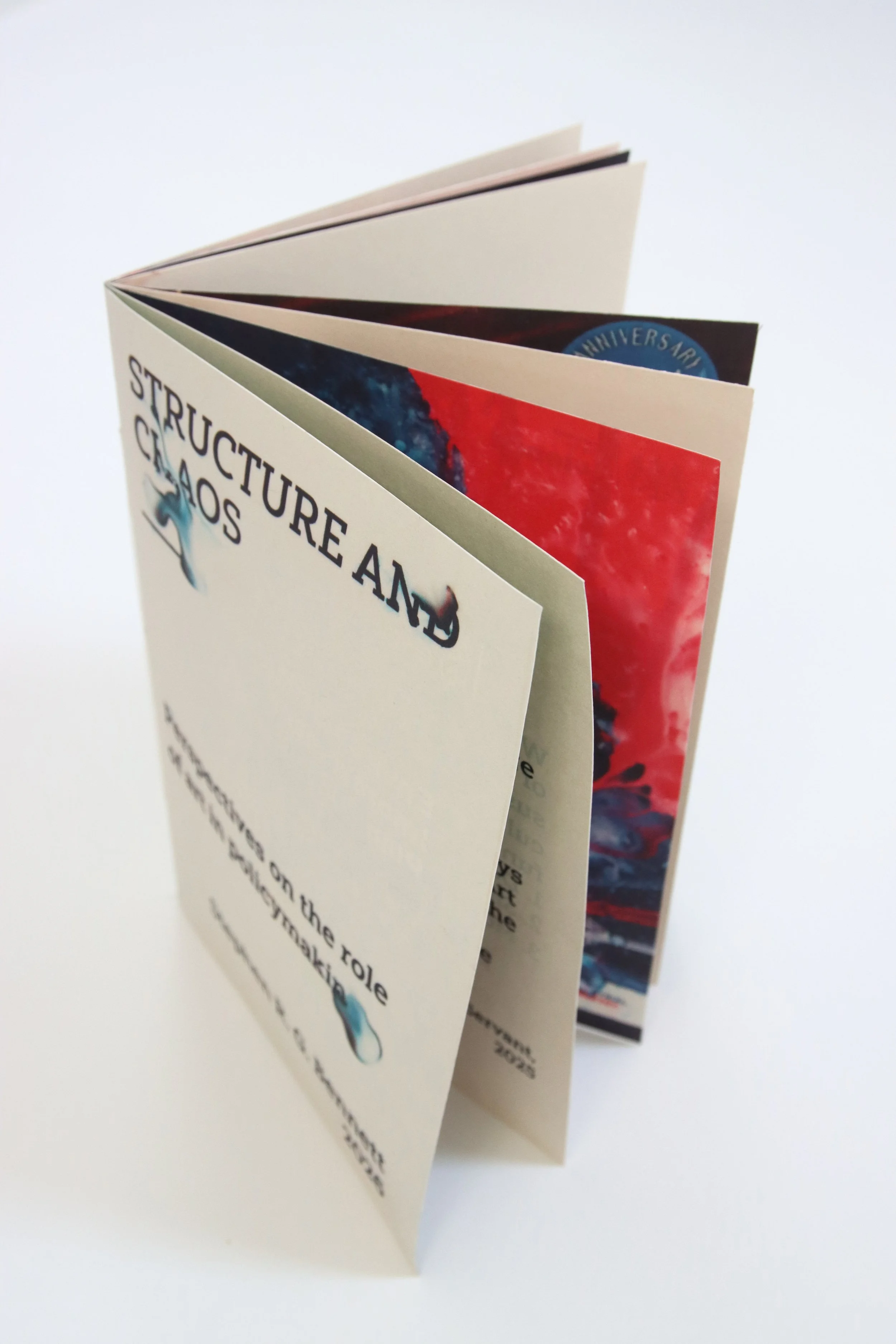 Structure and Chaos artist book standing partly open, showing its cream cover and red and blue internal pages.