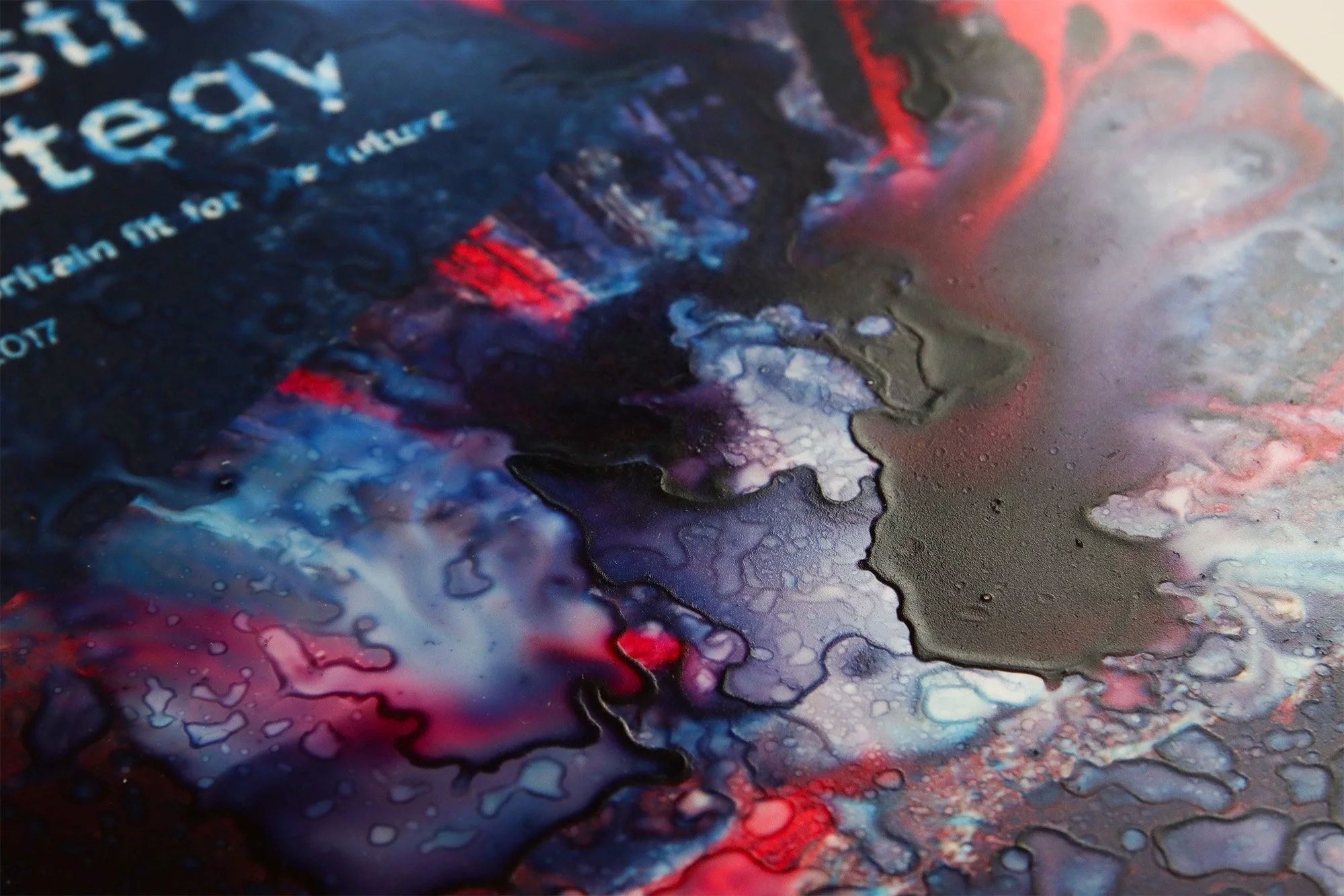 Close-up of the altered Industrial Strategy print showing pooled blue, black and red ink, water marks and disrupted printed text.