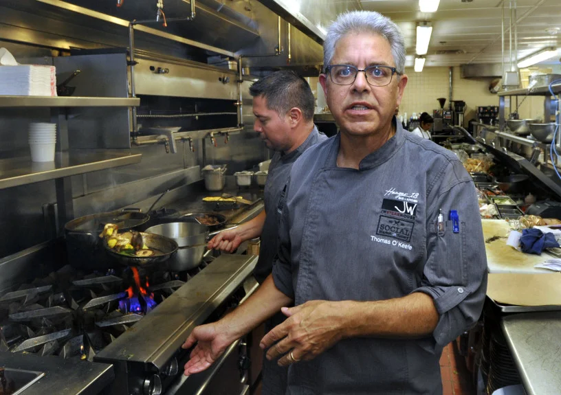 Executive Chef Thomas O’Keefe speaks while Executive Sous Chef Victor Miguel cooks in the background in the kitchen of Social Market and Eatery at the Los Angeles Airport Marriott Hotel, Thursday August 2, 2018. (Mike Mullen, Contributing Photographer)