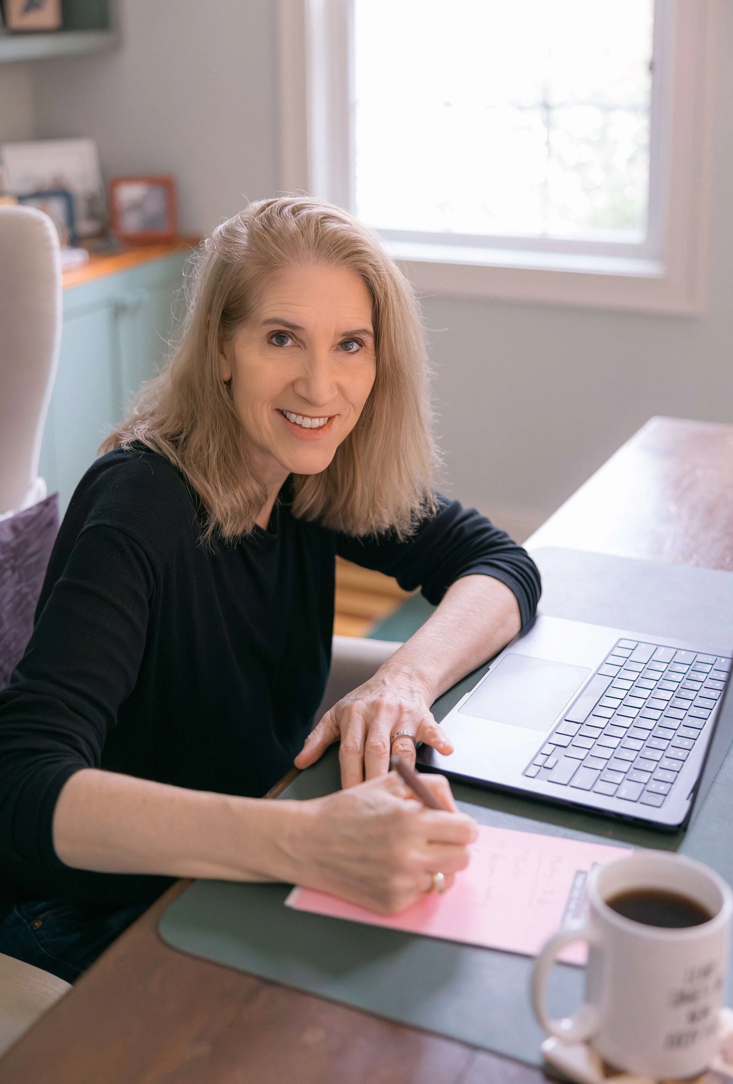 Catherine writes at her desk, smiling into the camera