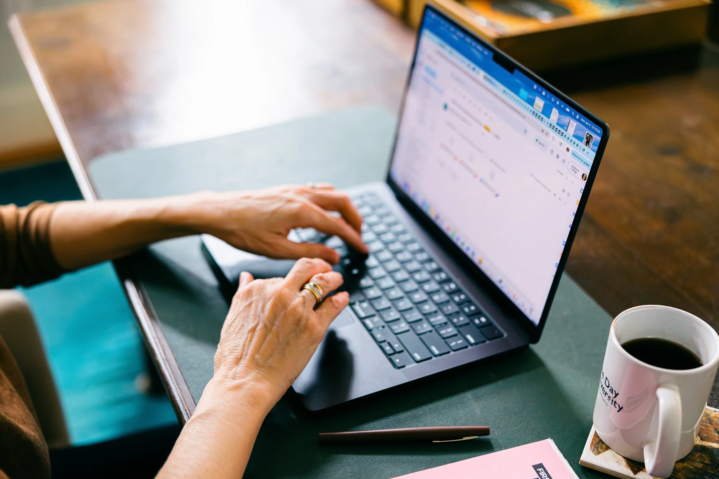 Catherine types at her laptop on a wooden desk