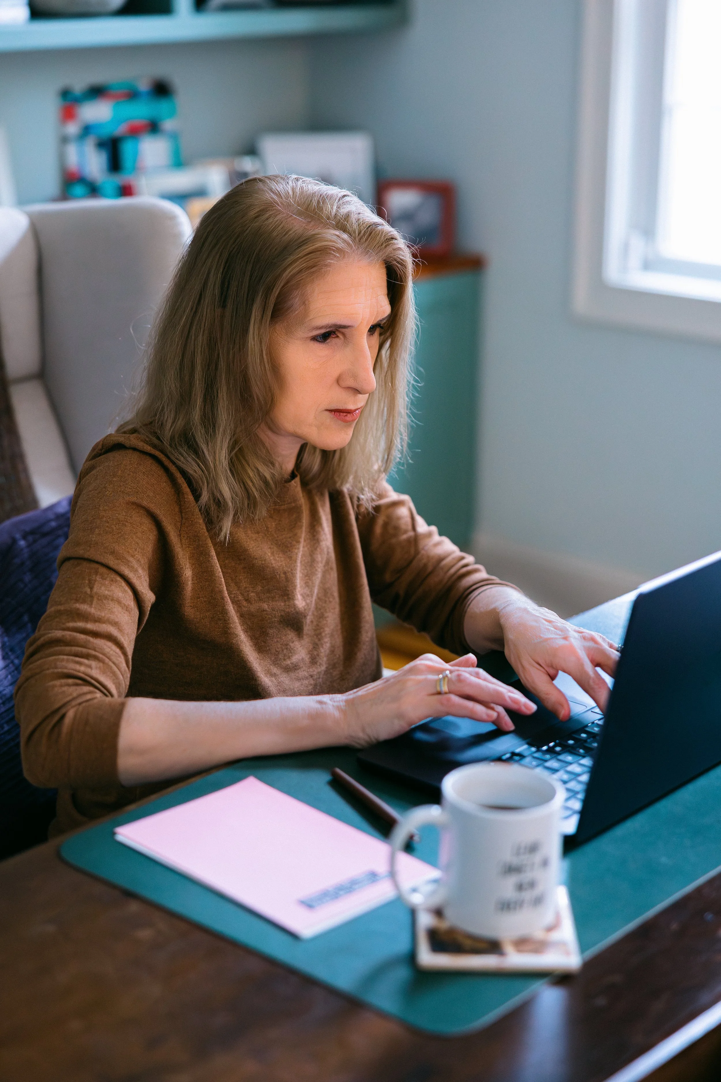 Catherine types at her desk in a brown sweater