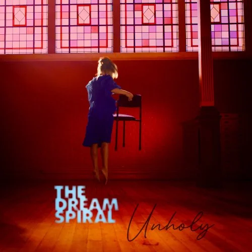 A young girl in a blue dress stands on a chair in a dimly lit room with stained glass windows, lifting the chair. The image the cover of the The Dream Spiral's Unholy album