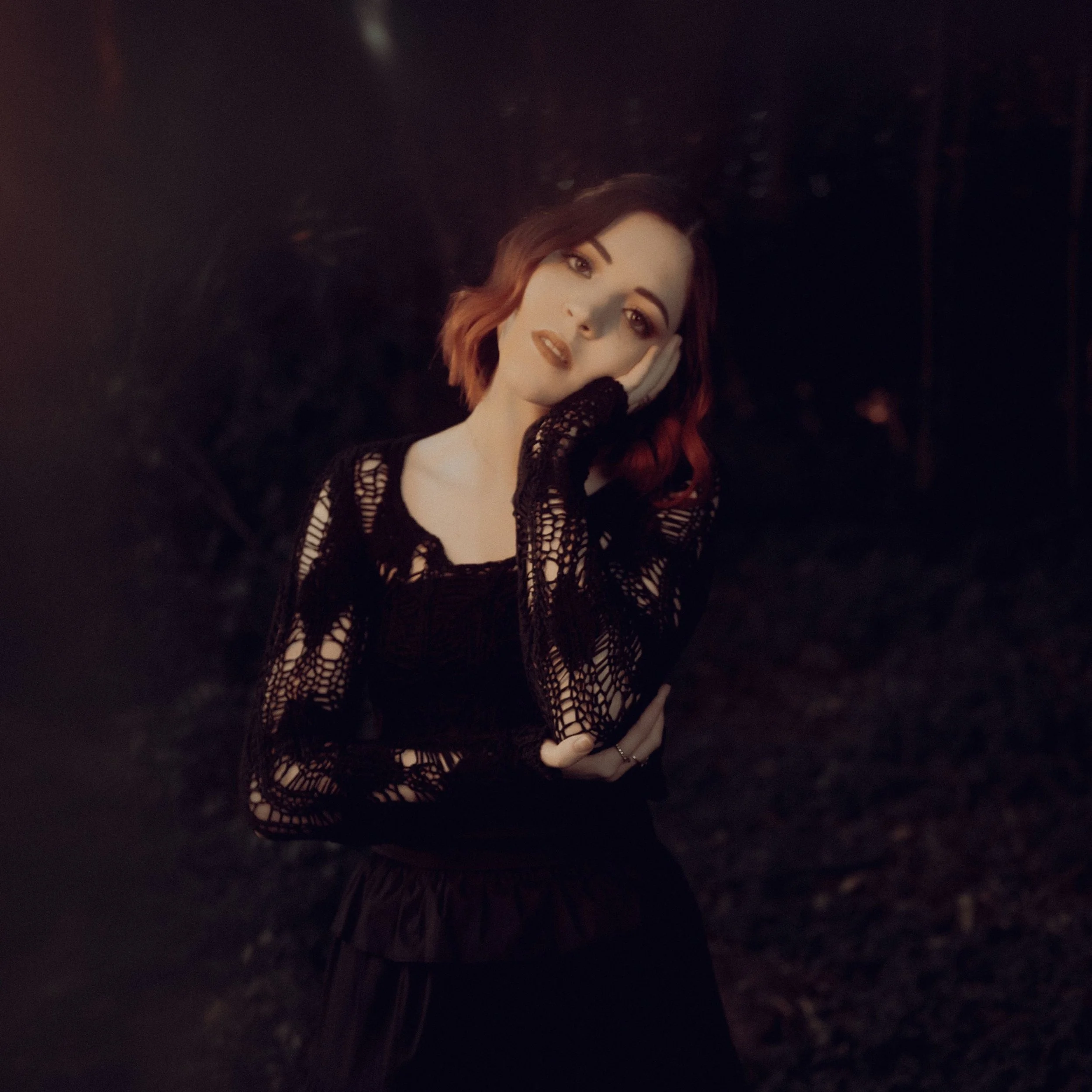 A woman with red hair in a black lace top against a dark background.