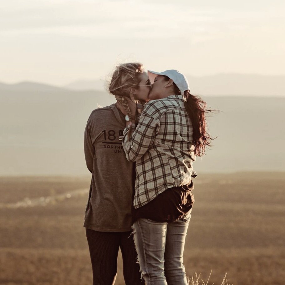 Gay Female Couple kissing in front of yellow horizon.png