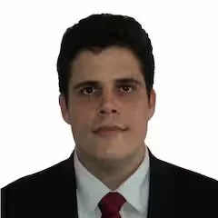 A man with dark hair wearing a suit and tie, against a white background.