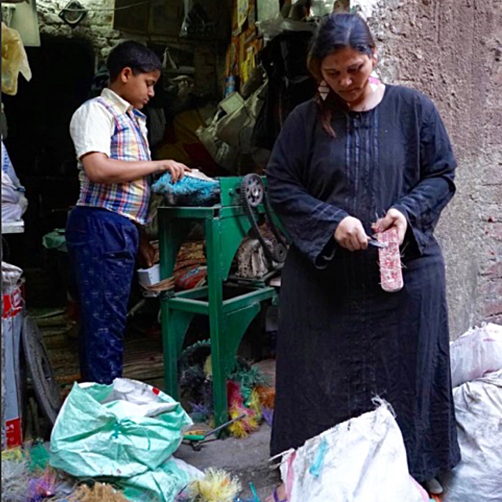 Mariam* bought discarded brooms and invested in a bristle-removing machine which her son is demonstrating. She then trims up the hard plastic base pieces which are valuable for recycling.
