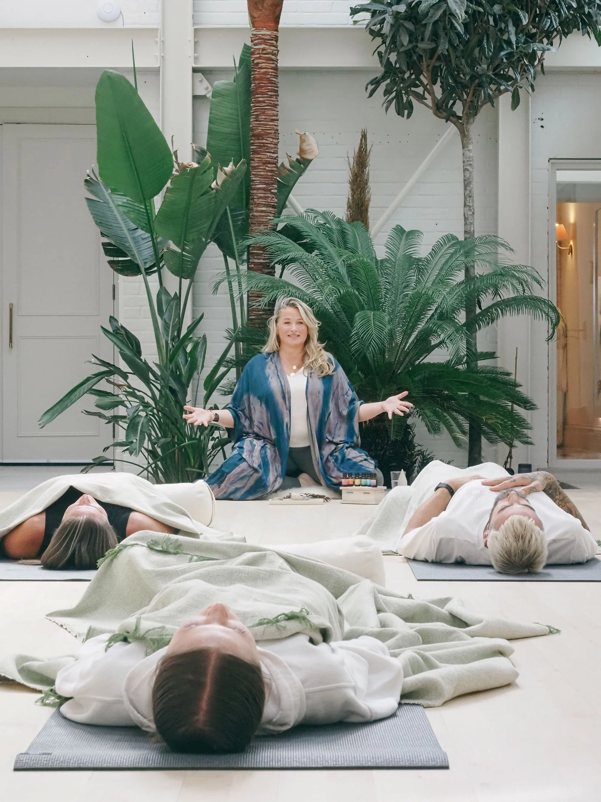 Ellie Loves leading a guided breathwork session with participants resting on mats in a bright, plant-filled studio, SuStudio, Canford Cliffs.