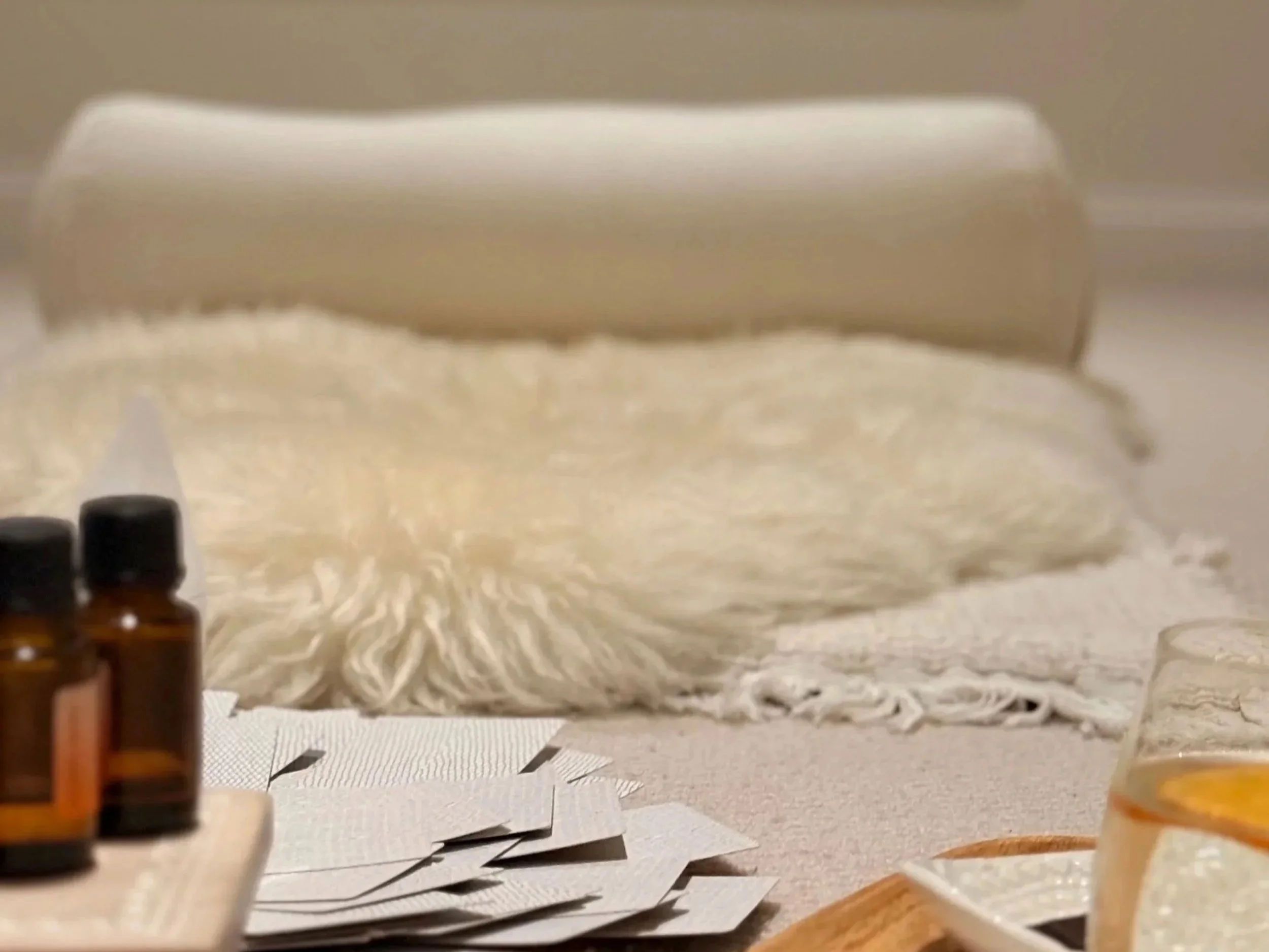 A close-up view of essential oil bottles and a white diffuser on a light-colored surface with paper sheets underneath, and a beige blanket in the background.