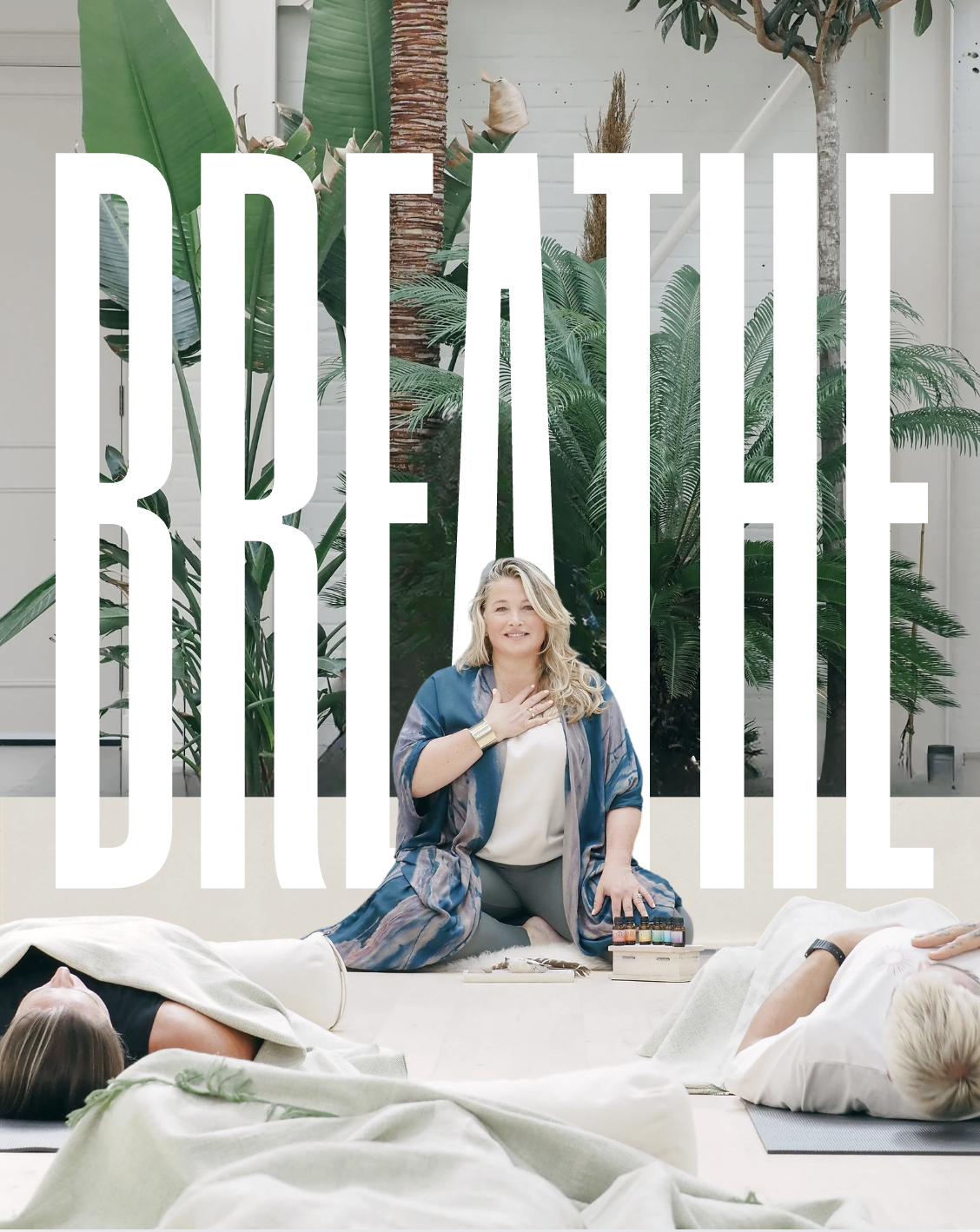 A woman leading a yoga or meditation class, sitting cross-legged on the floor with her right hand on her chest, surrounded by lush indoor plants, with two students lying on yoga mats with towels over them in front of her, and large white letters spelling 'JOE ANNE' over the scene.