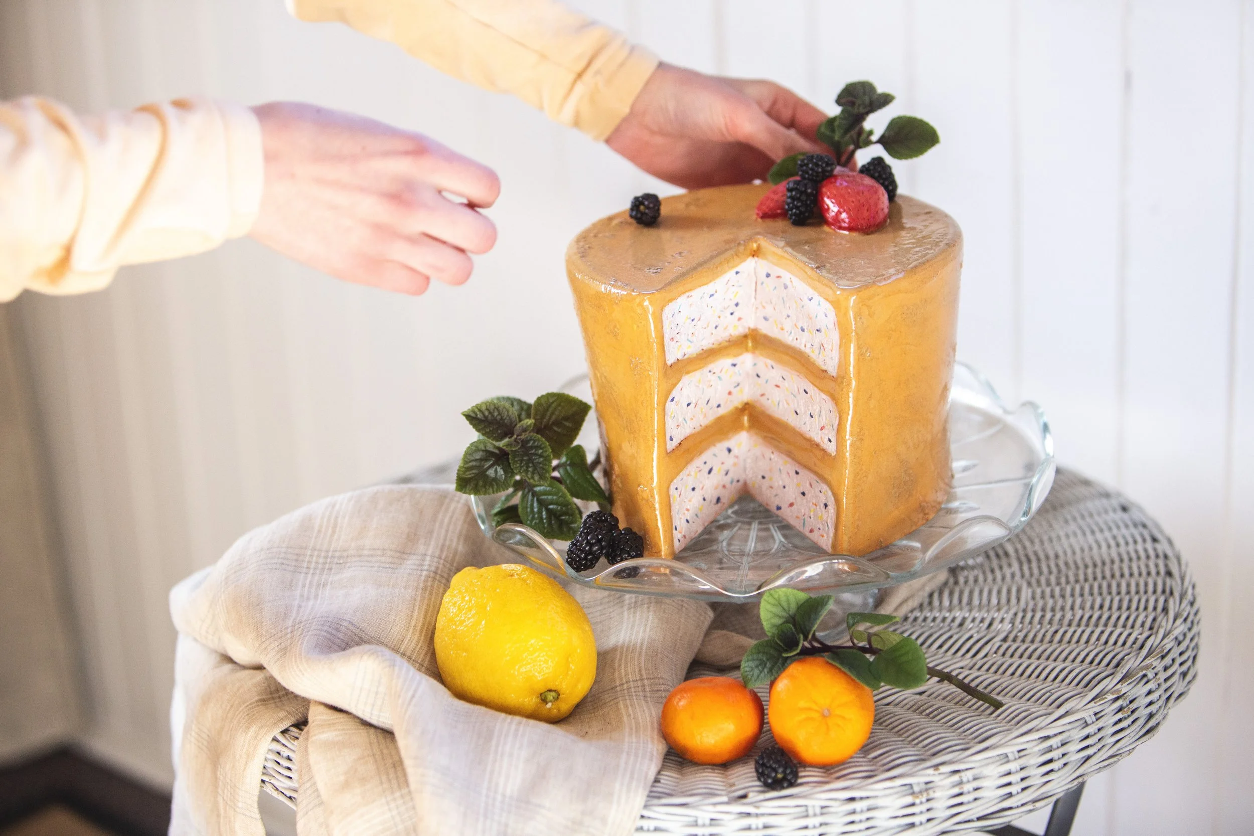Hands decorating a ceramic cake on a platter with fruit