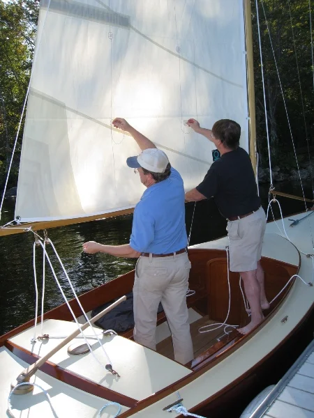 Bending on the sails. The sail is contained on the boom with a hand made Dutchman type system. 2mm Spectra lines are seized to the topping lift, woven through grommets in the sail, and terminated to bronze eye straps on the top of the boom.