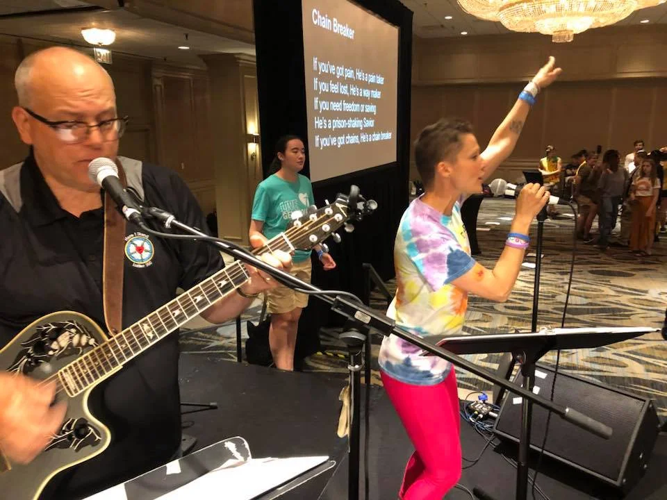 Pr. Mike Lembke on the left in the black shirt, playing guitar at this years Youth Gathering in Houston. His daughter, (on the right in Tie Dye T) Pastor Heidi Johnston leads singing.