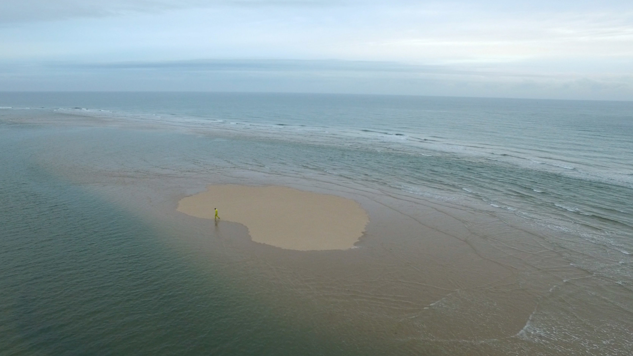 Simon Faithfull’s film, ‘Going Nowhere 1.5’ shows a lone man in a yellow suit walking doggedly around an intertidal island. We see the figure walk around the decreasing space, as the sea expands around him, until the sea is all we see.