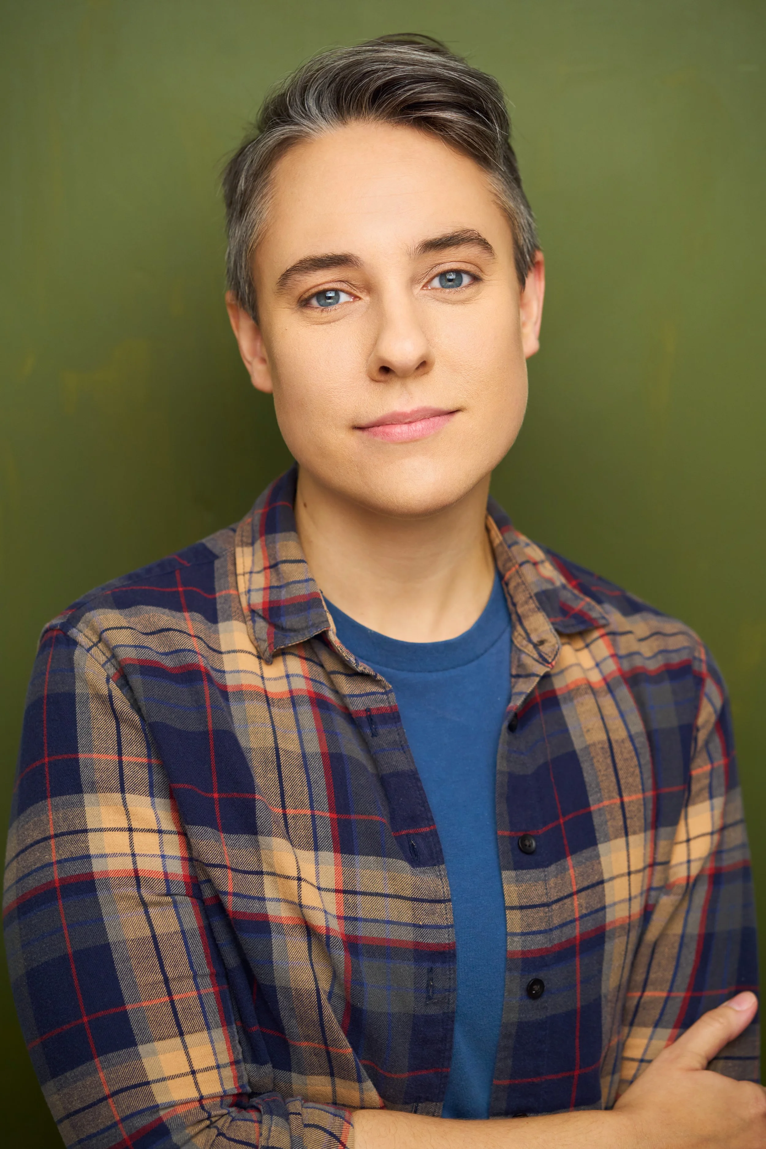 Dani Martineck, white transmasculine person with short graying hair, smiles at camera in blue T-shirt and plaid button-down