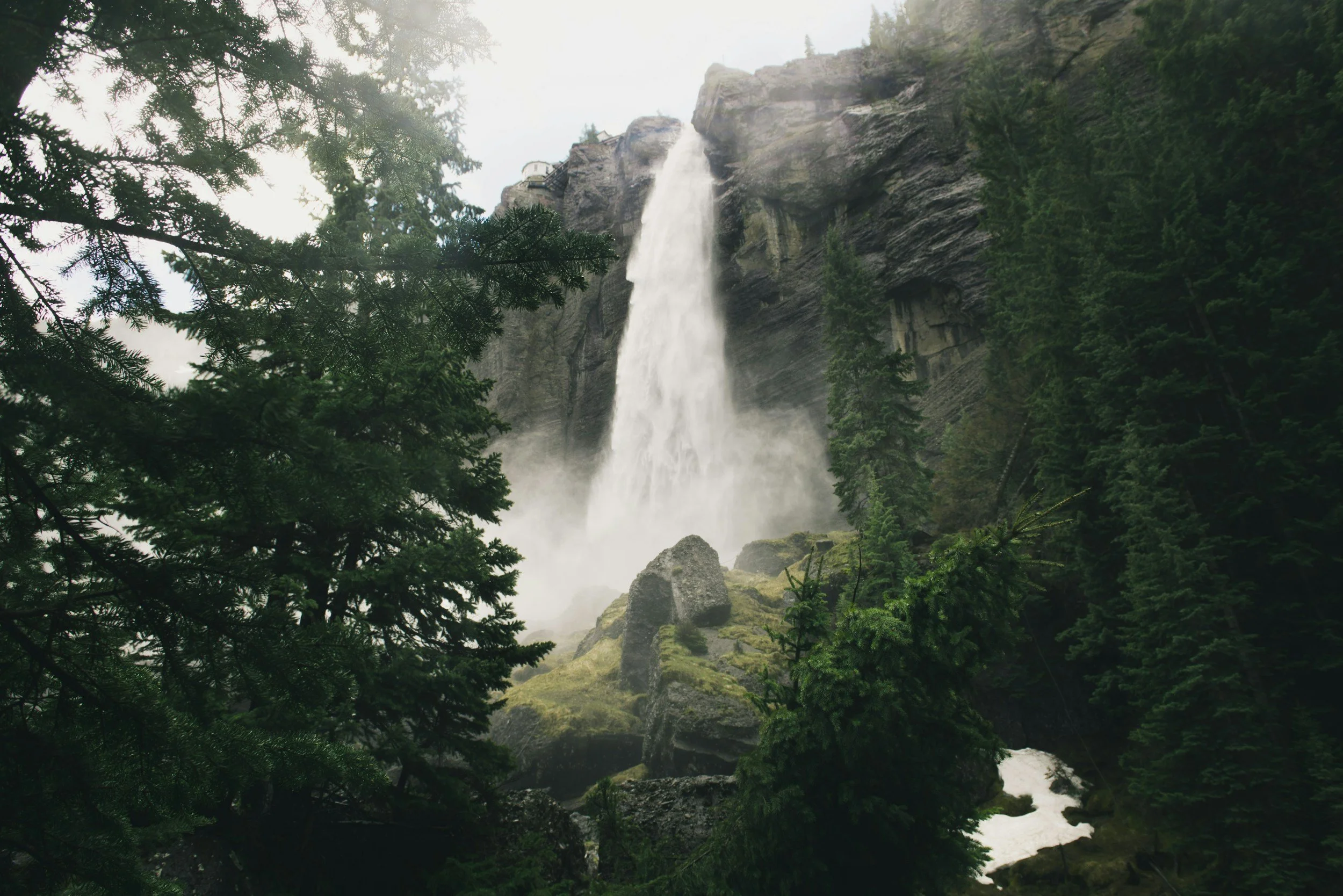 A waterfall cascading down a rocky cliff surrounded by lush green trees and moss-covered rocks.