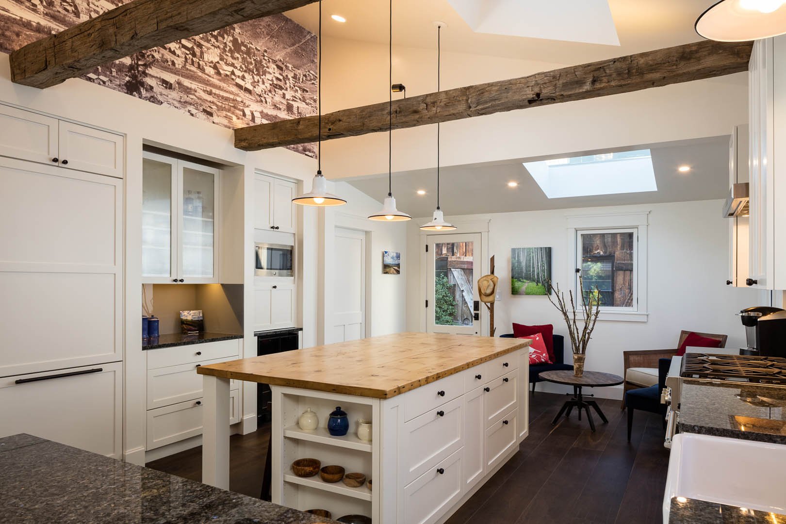 Modern kitchen with white cabinets, wooden island, pendant lights, exposed wooden beams, and nook with seating and artwork on the walls.