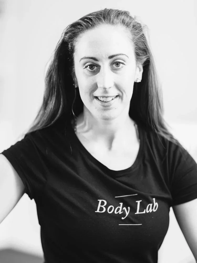 Black and white photo of a woman with long hair, smiling, wearing a t-shirt that says 'Body Lab'.