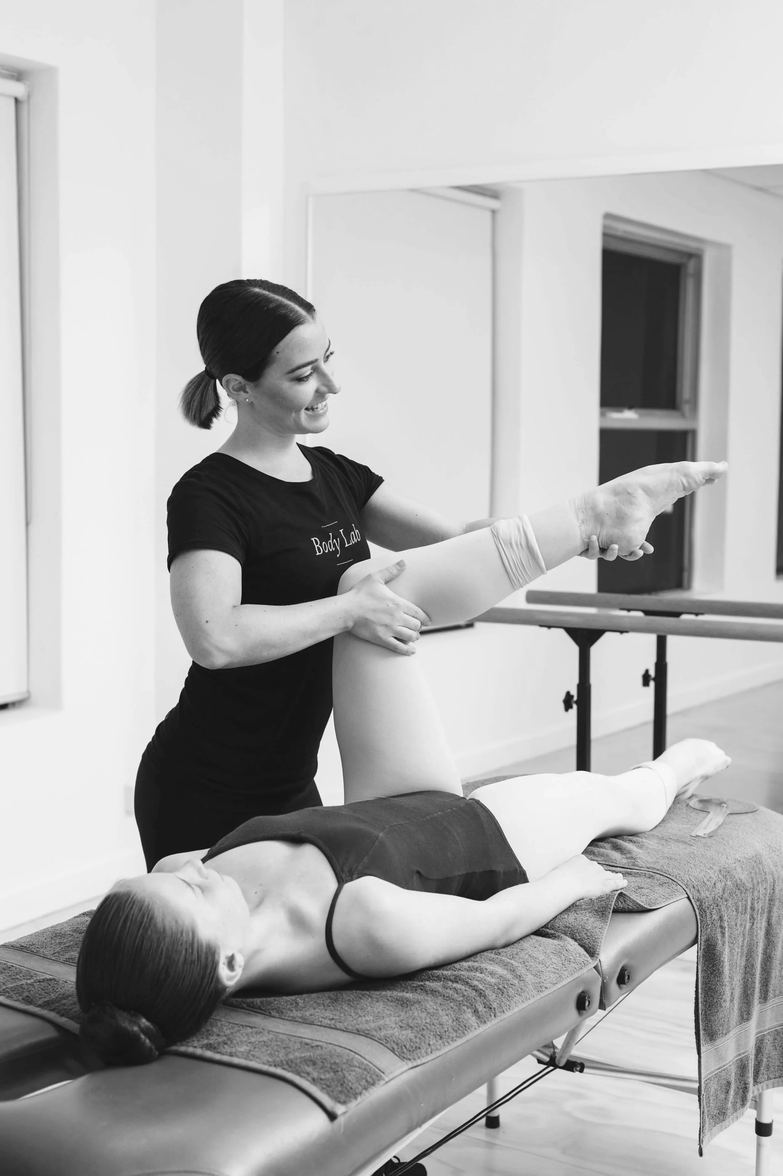A chiropractor or physical therapist assisting a woman with a leg stretch on a treatment table in a wellness clinic.