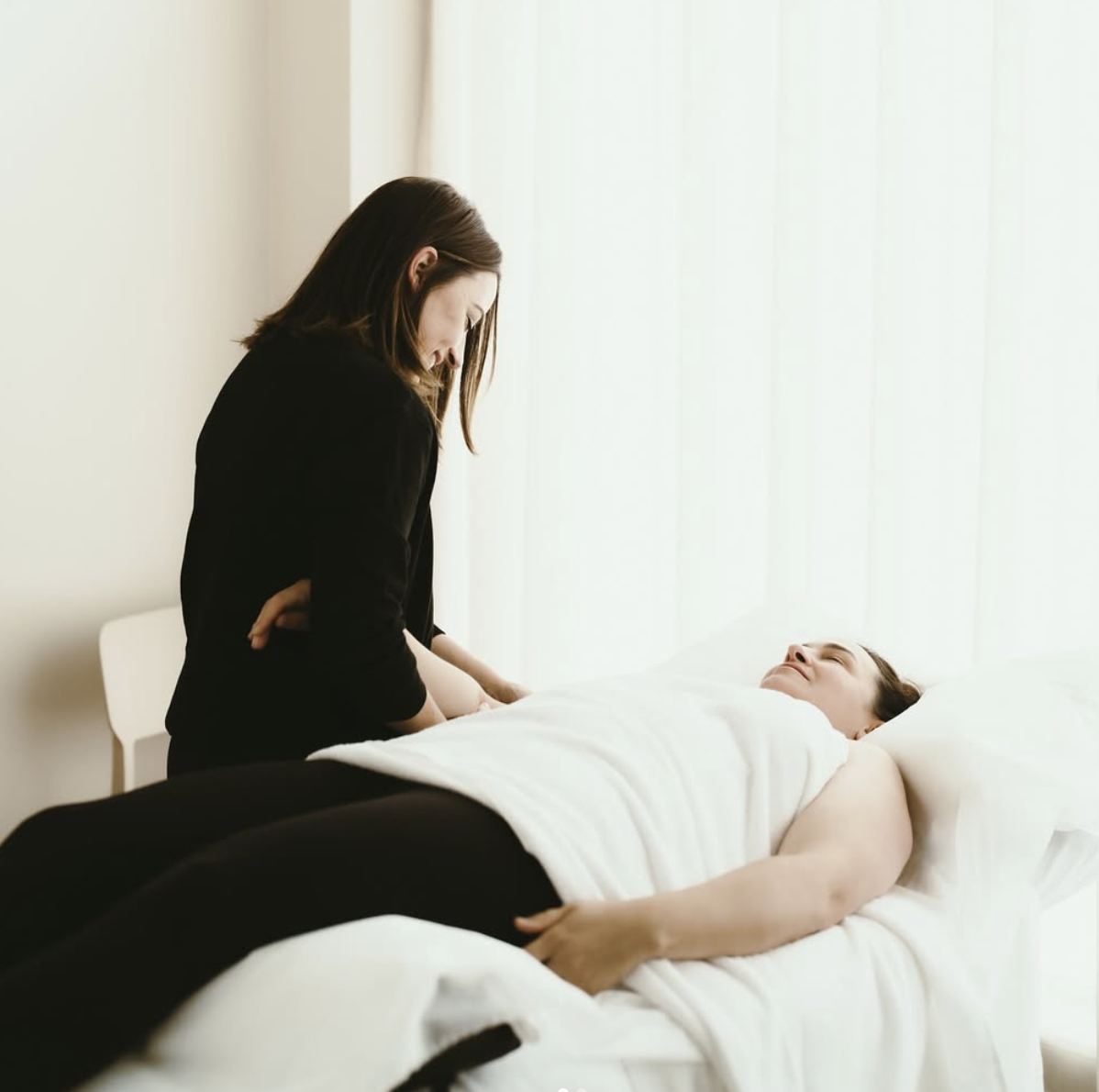 A physiotherapist leaning over a patient, in a bright clinic room with soft natural light.