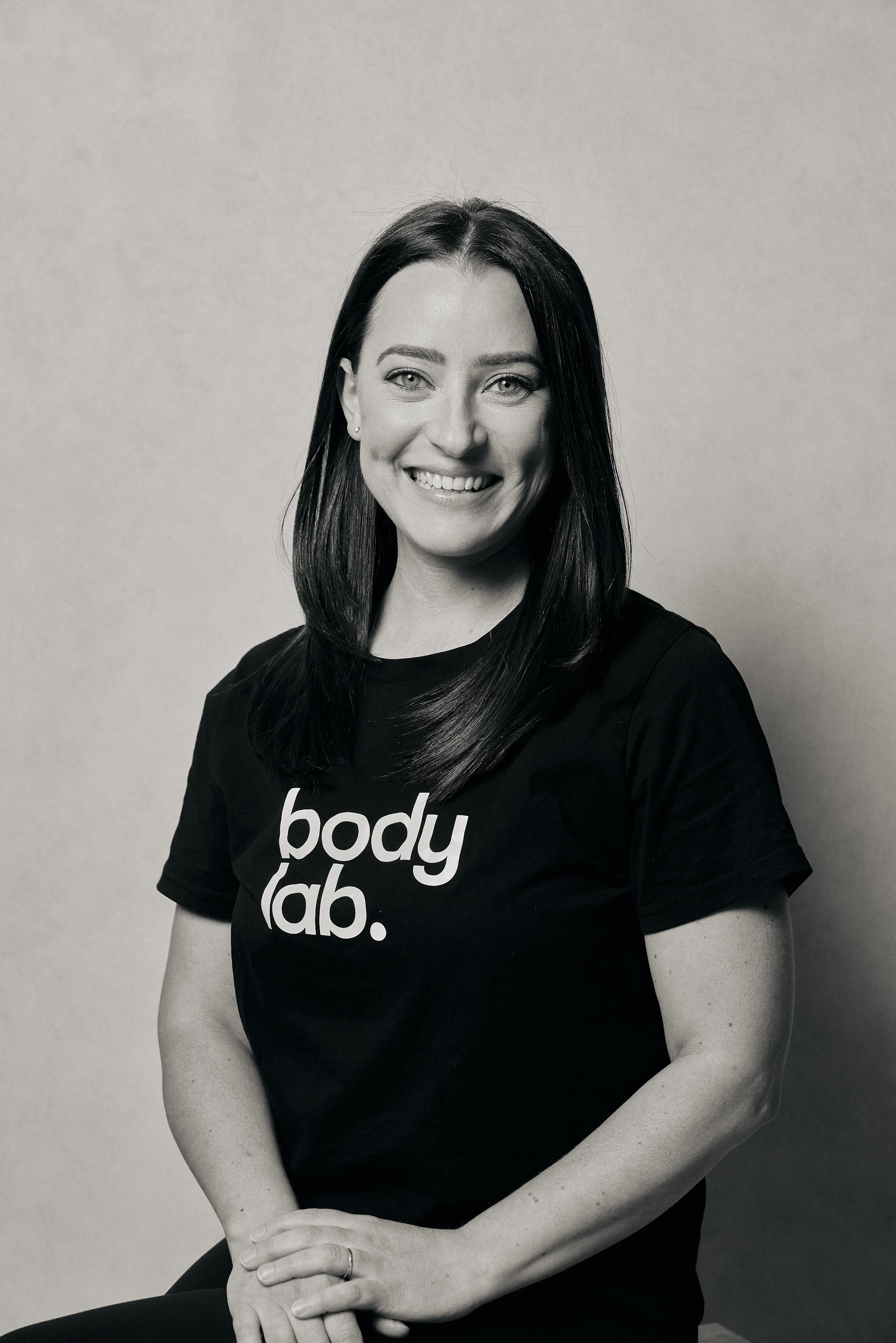 A woman with dark hair smiling, wearing a black t-shirt that says 'body lab.'