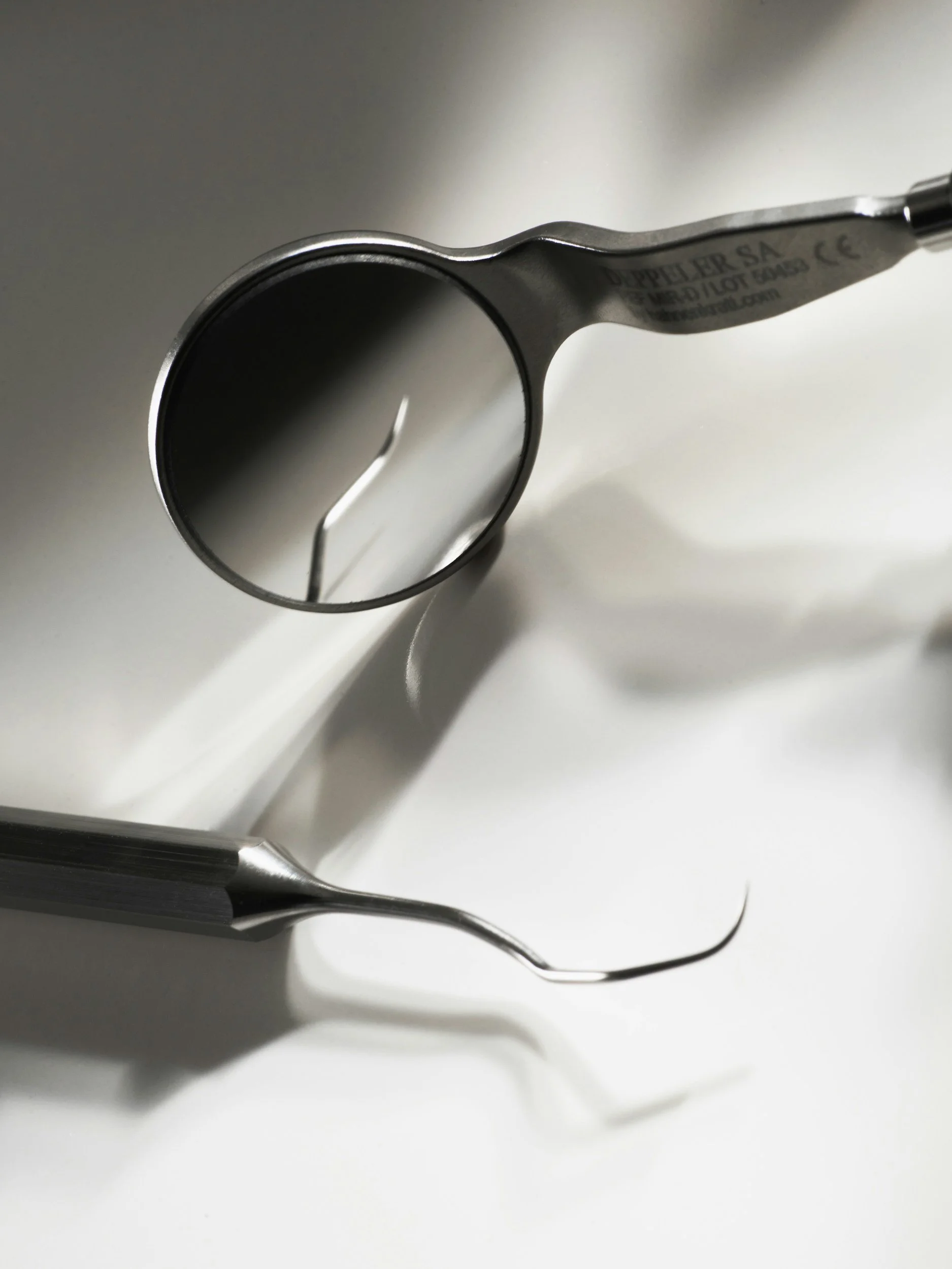 Close-up of dental tools, including a mirror and a scaler, on a white surface.