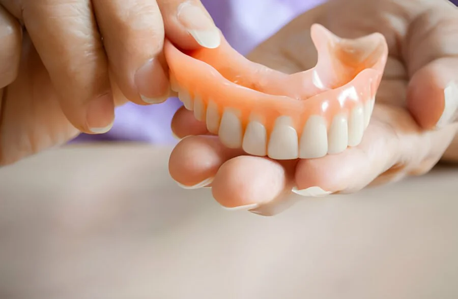 Close-up of a person holding a set of dentures with a pink gum base and white teeth.