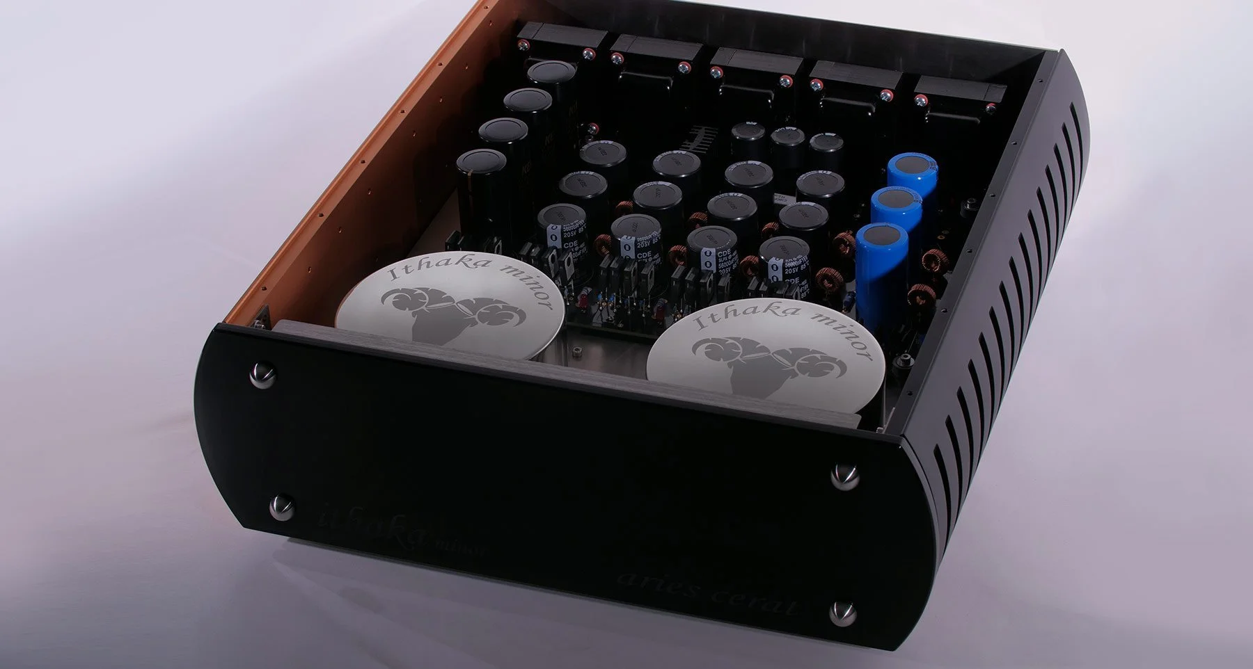 Close-up of two high-end audio devices labeled 'Kassandra'; the top device labeled 'Kassandra' features a metal surface with black, curved lines, and the bottom device labeled 'Kassandra II Le' has electronic displays showing signal levels, all set on a dark wooden surface.