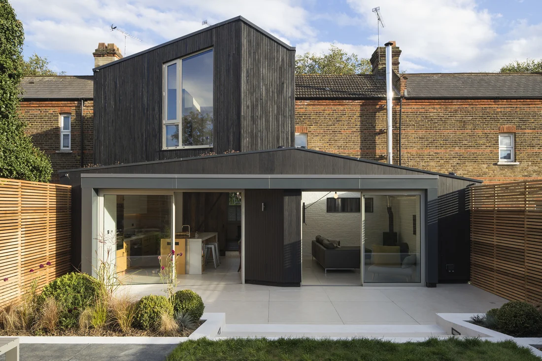 A row house extension in London (UK) by Neil Dusheiko whose firm regularly designs additions. Note the contrast between the old brick of the existing house, the black addition and the clean lines of the garden layout. This addition allows for a modern kitchen and sitting area as well as an extra room on the first floor. Artfully done.