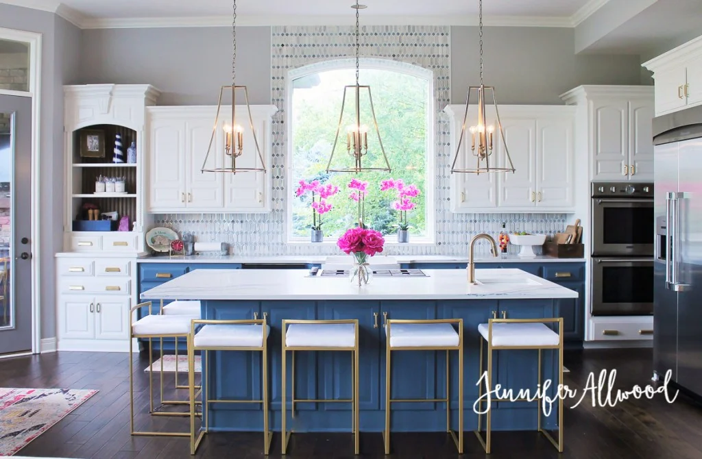 Typical contemporary North American kitchen with lovely brass accents and colour on the base cabinets! Note how the backsplash tile is carried around the arched window giving it emphasis. Design by Jennifer Allowed.