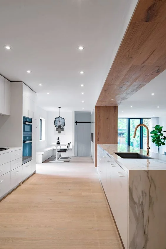 I like how the sink block in this kitchen is defined by the wood gable at the far end cabinetry which is then carried on to the ceiling and over the sink block. This wood detail adds a lot of warmth to an otherwise cool feeling kitchen. Note all the recessed pot lights in the ceiling providing lots of general lighting together with a funky chandelier fixture over the dining table in the nook. Source: Studio AC (Netherlands)