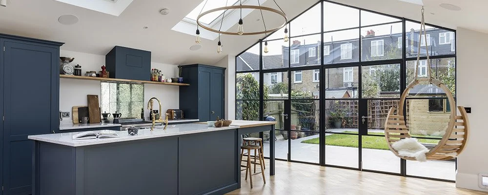 Beautiful kitchen extension with a full wall of contemporary black framed glass windows and doors opening to a small urban garden. Skylights add even further light making the space look large and open. Source: Proficiency Ltd. (UK).