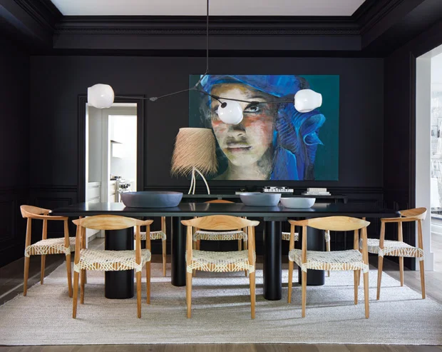 Note how the tall baseboards and the door casings have been painted out in black as well. As is the ceiling! The light colour of the wood floor, the rug and the chairs immediately adds warmth to the space. The clean white lamp shades of the ‘chandelier’ reflect the white in the adjacent rooms, while the cobalt blue of the artwork adds a touch of colour to the space. All these elements contrast wonderfully while at the same time forming a coherent look. Design by Montana Burnett and Hailey Atkins.
