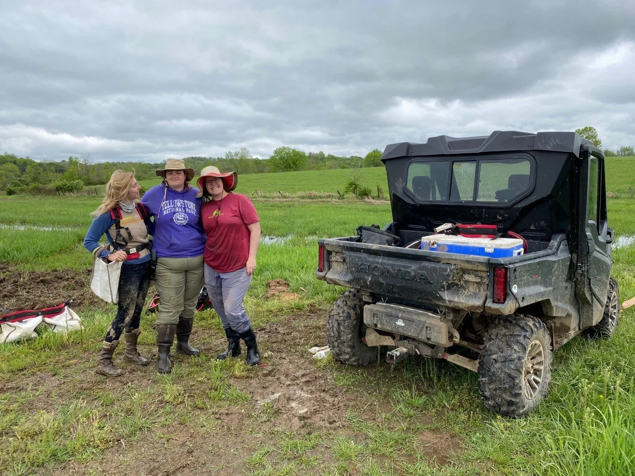 Three people pose next to ATV in a field.
