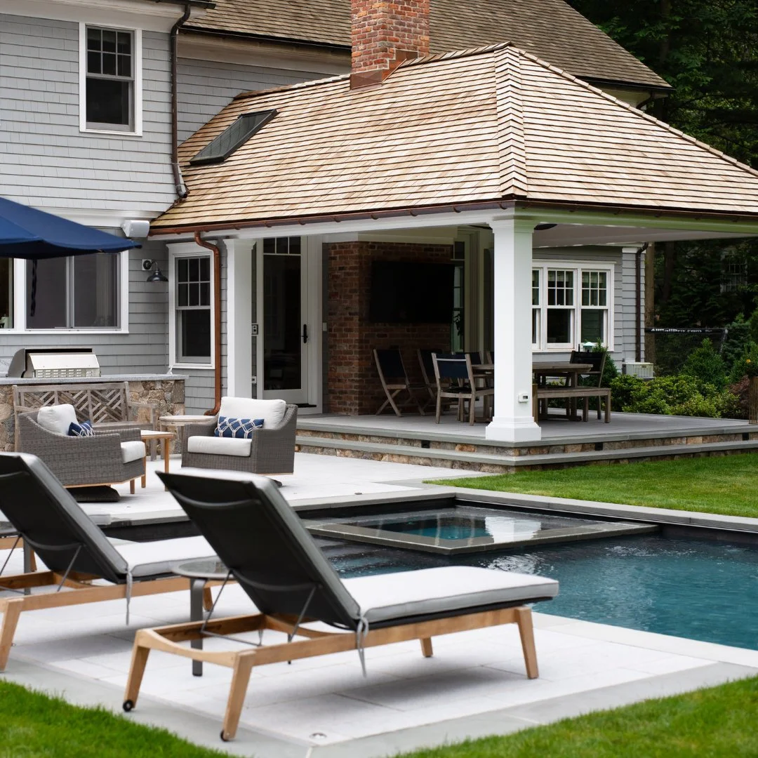 The perfect backyard for entertaining, featuring a beautifully crafted Marsh Grey Porcelain patio surrounding a pool, hot tub, outdoor kitchen, and pergola - creating a seamless space for relaxing and hosting in style.