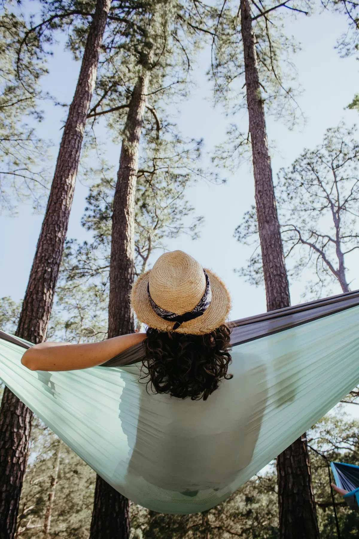 Woman in straw hat resting in a hammock surrounded by tall pine trees, enjoying rest and renewal on a career break