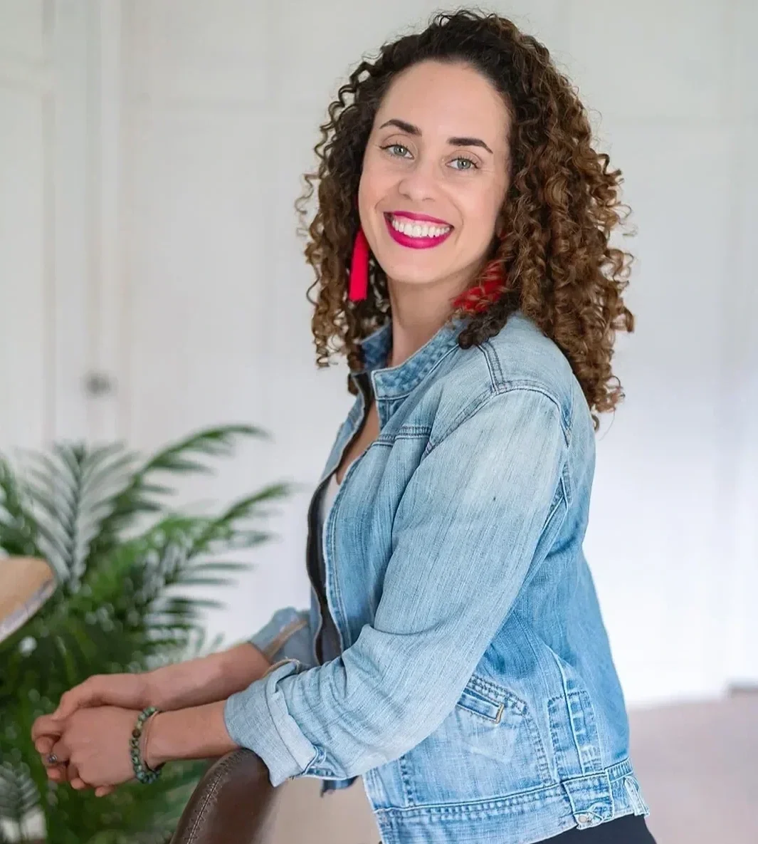 Katrina McGhee sabbatical coach smiling over shoulder in a bright airy studio with palm plant
