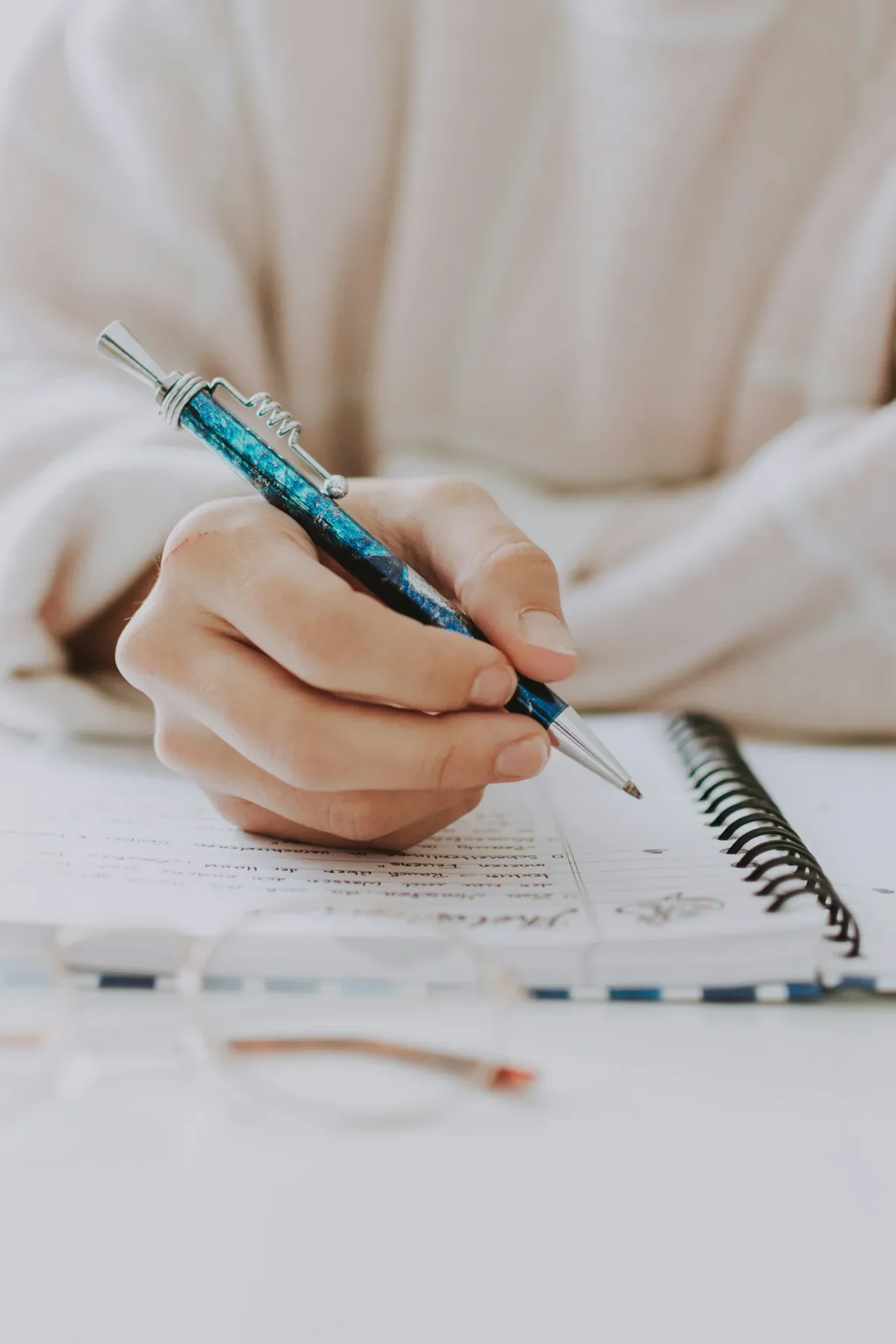 Close-up of a hand writing in a spiral notebook with a teal pen, evoking intentional planning during a career break