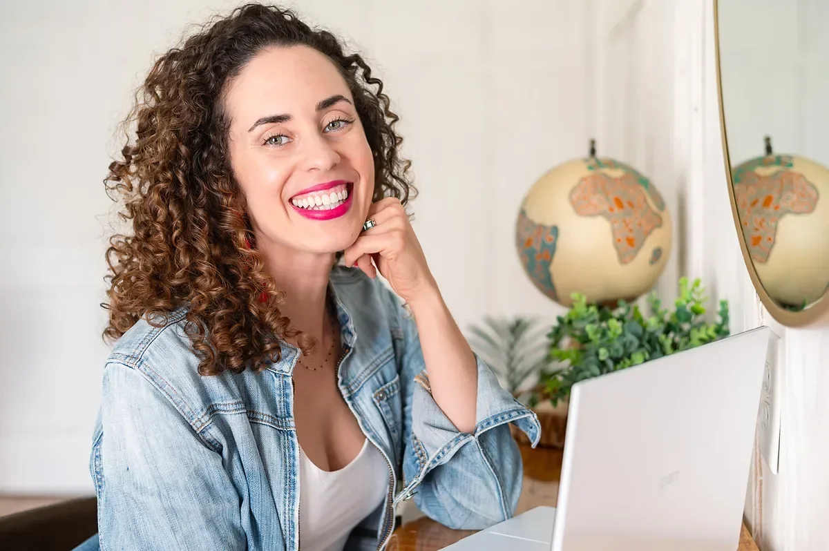Career break coach Katrina McGhee laughing joyfully in denim jacket at her desk with globe in background