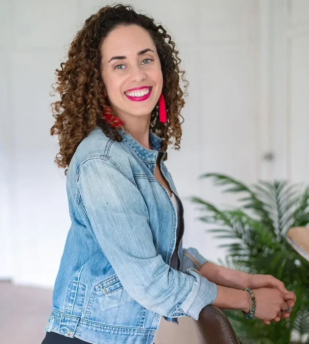 Katrina McGhee sabbatical coach smiling over shoulder in a bright airy studio with palm plant
