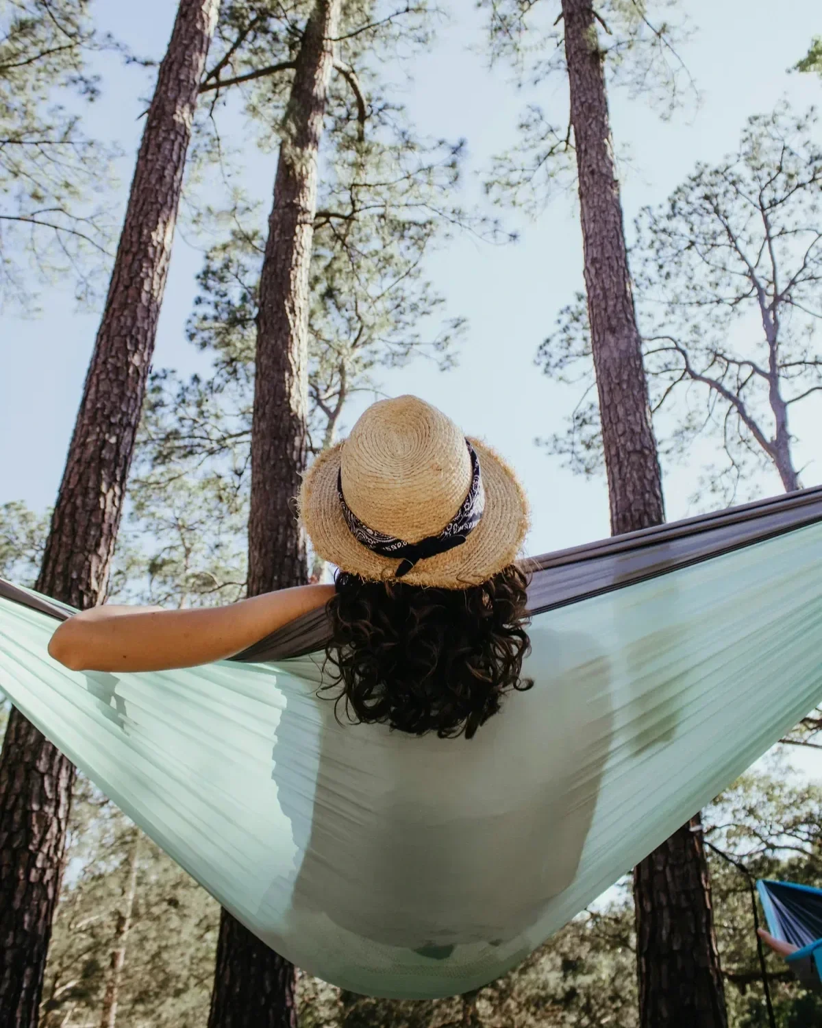 Woman in straw hat resting in a hammock surrounded by tall pine trees, enjoying rest and renewal on a career break