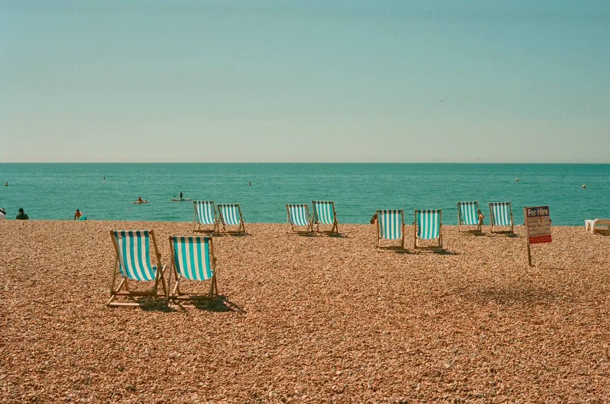 Teal and white striped deck chairs on a pebbly beach with calm ocean in the background, evoking leisure and career break relaxation