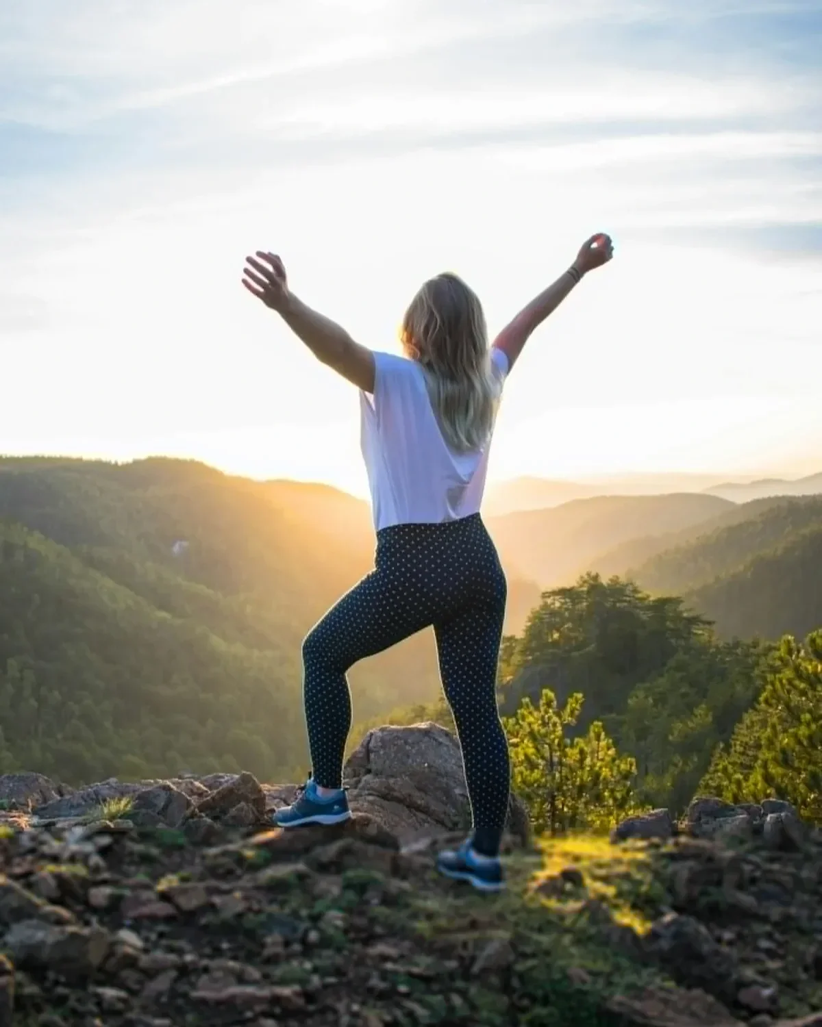 Woman with arms raised in celebration on a mountain summit at golden sunset, symbolizing freedom and career break triumph