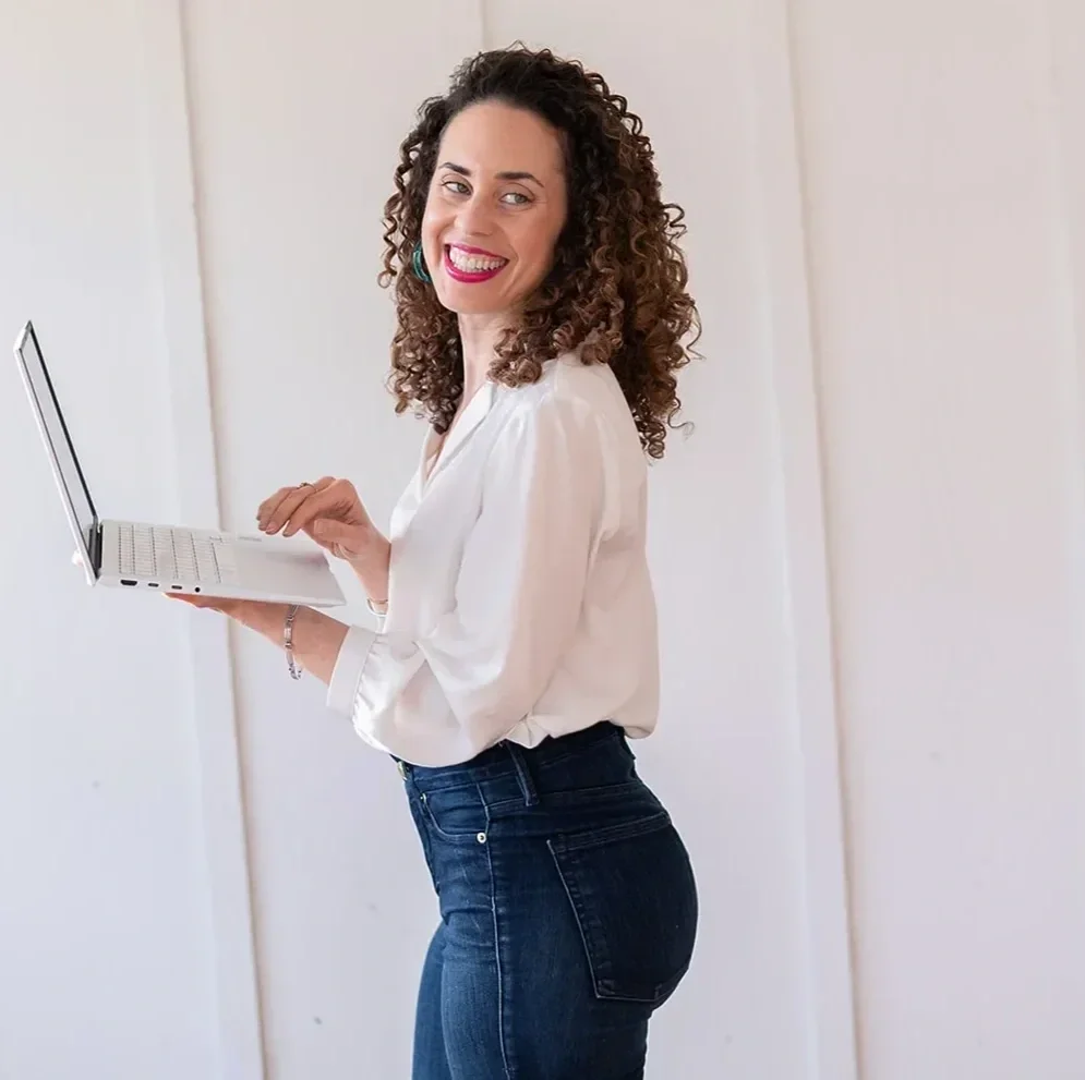 Katrina McGhee standing holding open laptop, smiling over shoulder against white background