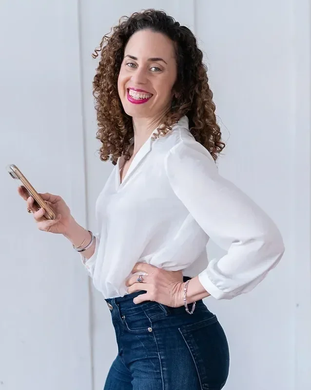 Career break coach Katrina McGhee in white blouse smiling over shoulder while holding a phone